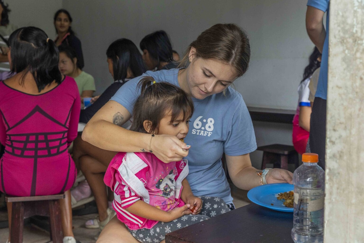 A 6:8 staff member feeding a little girl at a feeding center
